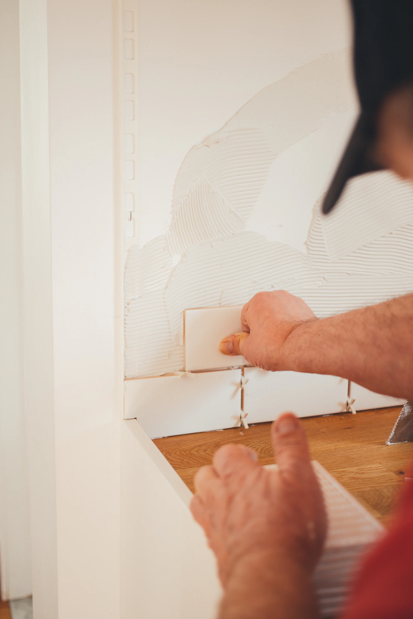 A pair of gloved hands pressing a fresh sheet of drywall against a stud wall
