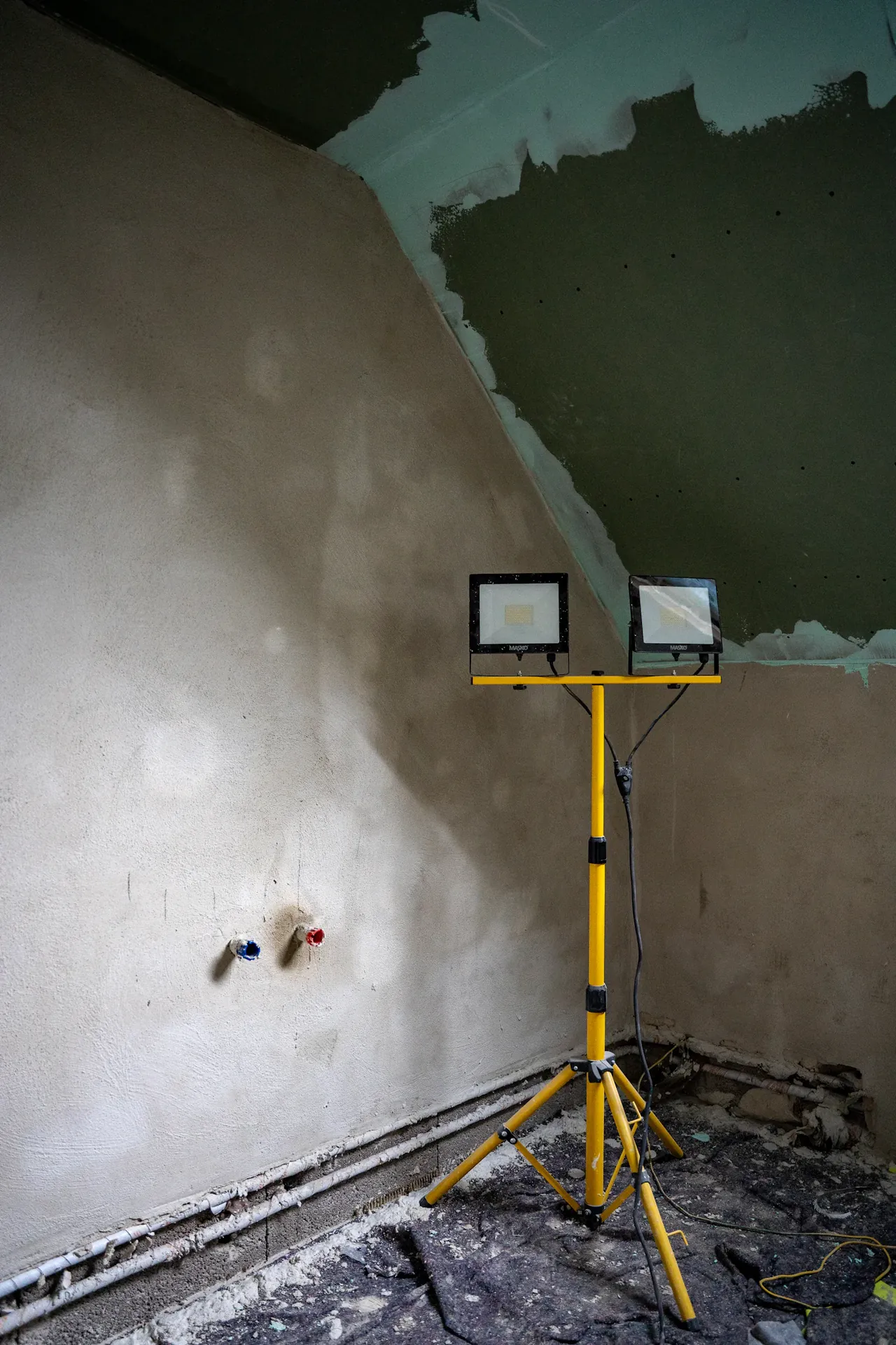 An interior with drywall hung and taped, lit by temporary site lighting
