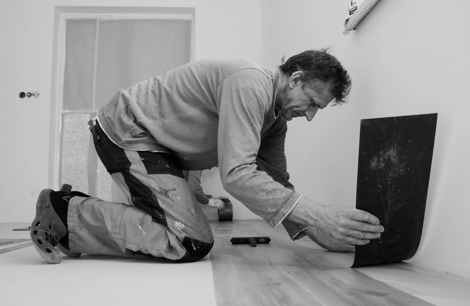 An installer working at floor level, fitting planks along a wall