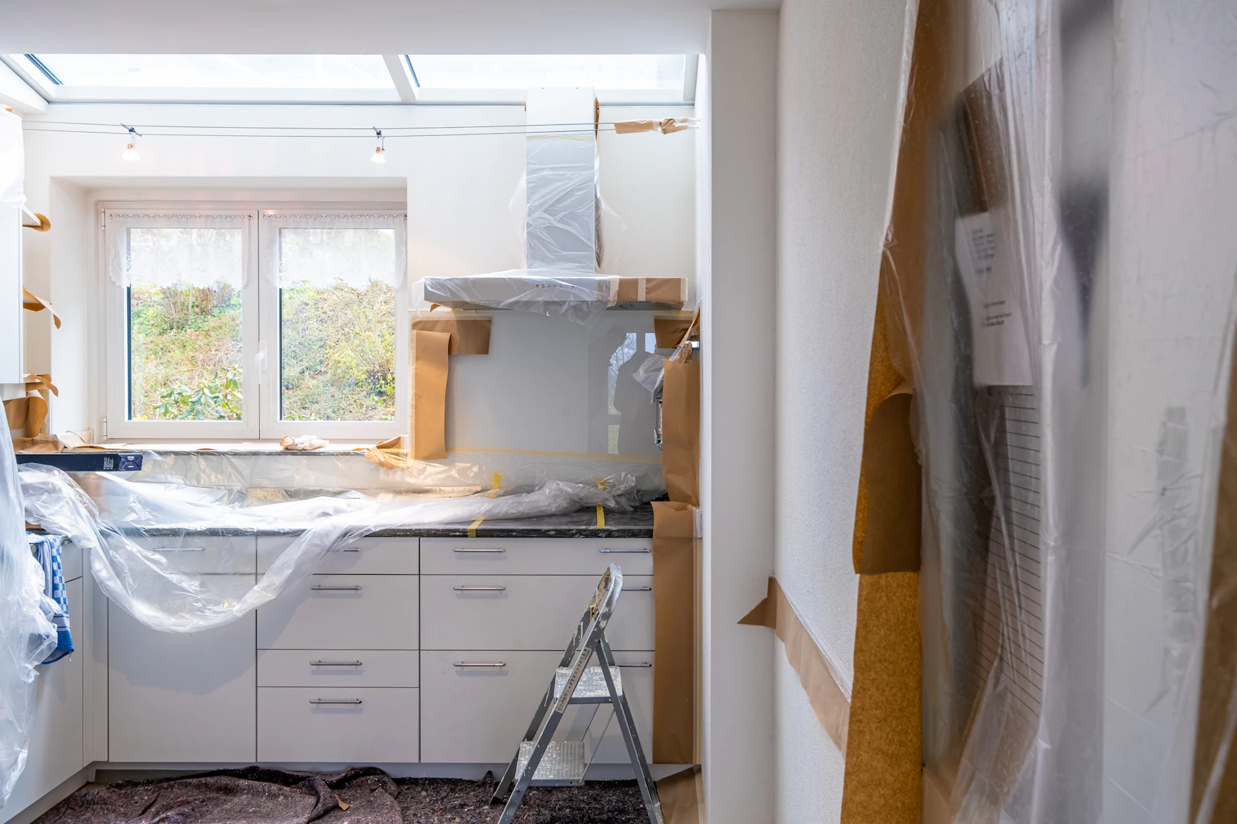A kitchen part-way through a renovation, new cabinet boxes set and masked off behind paper and plastic