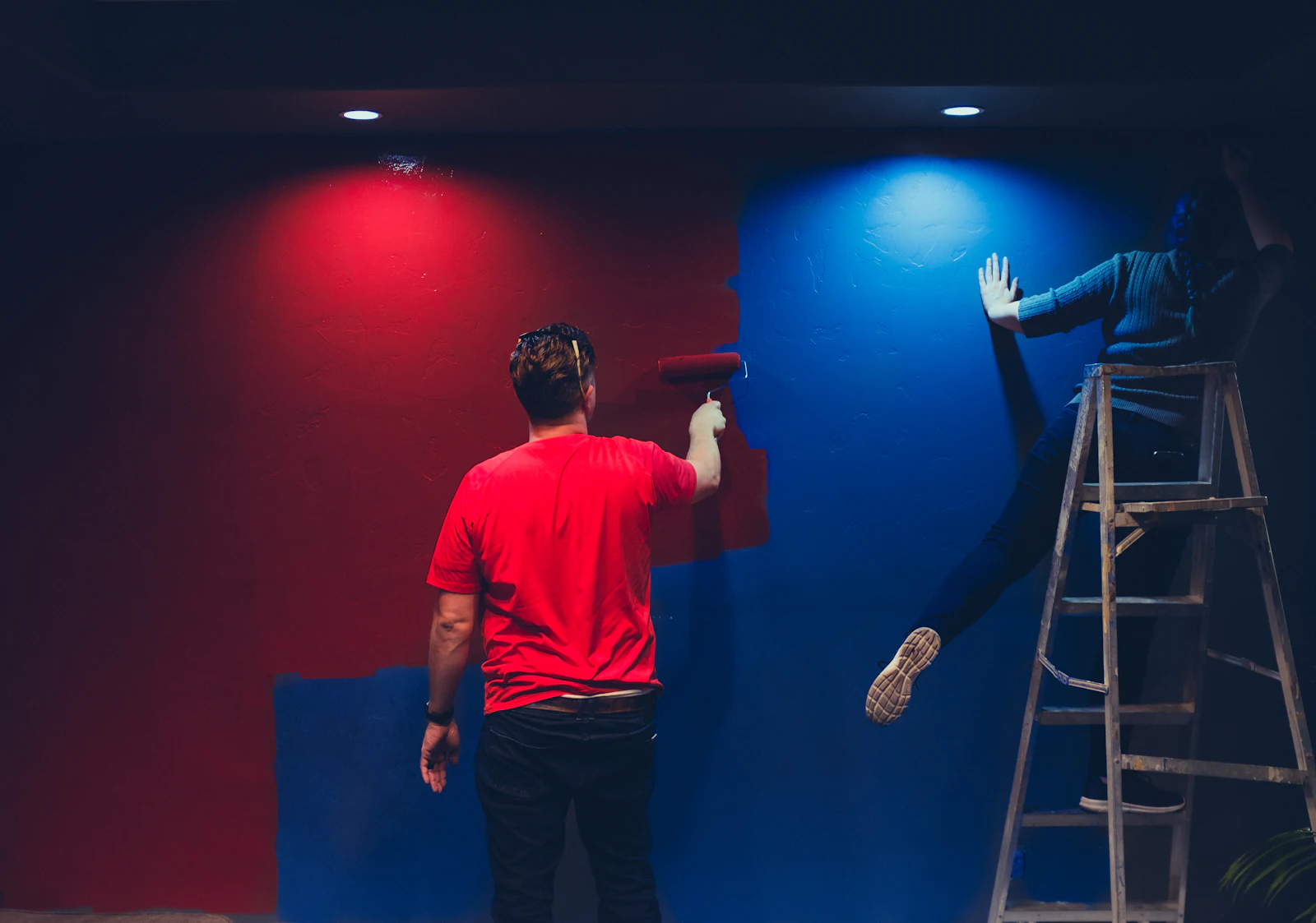 Two people rolling paint onto a wall in an empty room