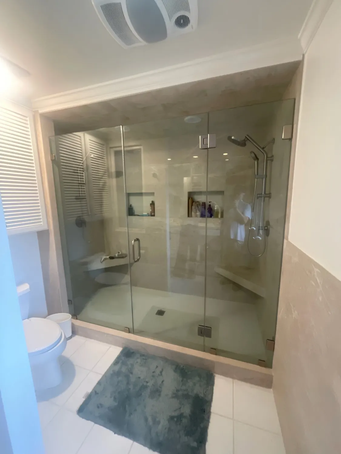 A finished bathroom with a frameless glass shower enclosure in stone-colored tile, a built-in bench and a recessed niche