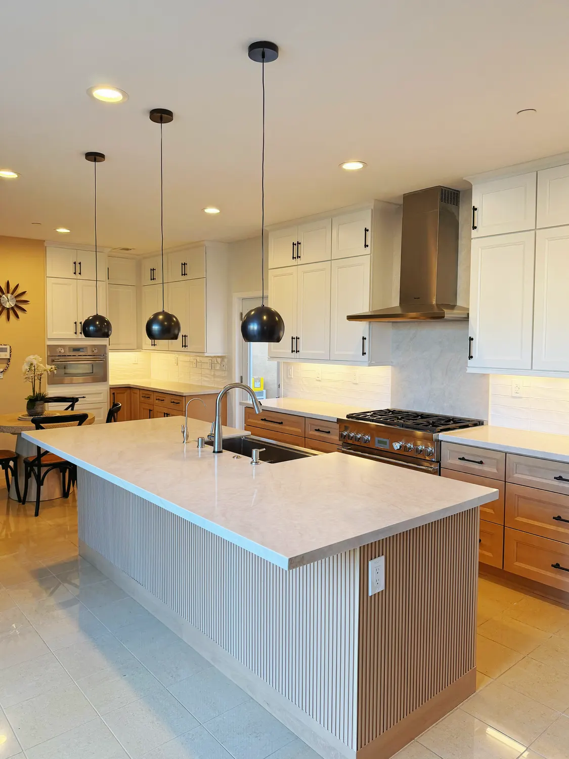 A kitchen island with a fluted oak base and a pale stone top, three black globe pendants hanging above it